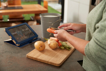 Woman with tablet PC peeling carrot preparing meal at home