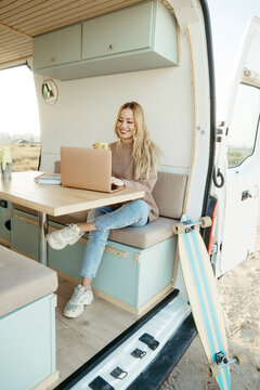 Happy digital nomad working on laptop sitting inside motor home