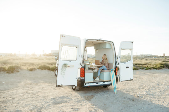 Young freelancer sitting with laptop in caravan in front of clear sky
