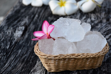 Fototapeta na wymiar Soft focus of Alum cubes and plumeria flower on wicker basket, blurred background, concept for herb, bodycare, skincare, waterclear, spa, treatment, disease protection and protect armpit smell.