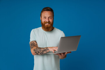 Ginger excited man with tattoo smiling and working with laptop