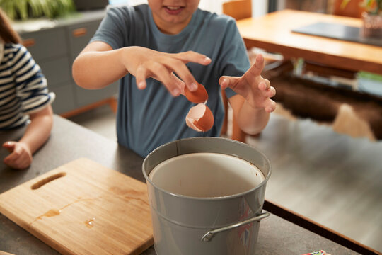 Hand of boy throwing egg shell in garbage bin at home