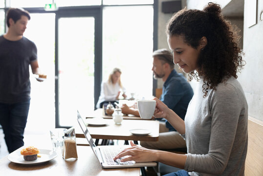 Smiling freelancer working on laptop drinking coffee at cafe - Powered by Adobe
