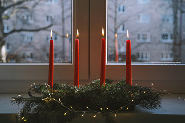 Burning red candles on advent wreath in front of window at home