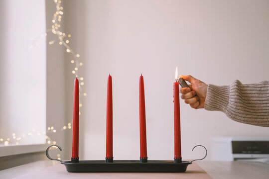 Woman burning red Advent candle with lighter at home - Powered by Adobe