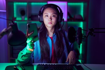 Young asian woman playing video games with smartphone relaxed with serious expression on face....