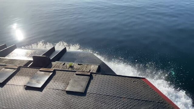 Ferry boat moving fast over perfect calm water. Water splashing over the bow of a car ferry. Sunlight reflections and lens flares while moving over water. Deep blue water of the lake of Constance. 