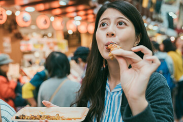 closeup of satisfied asian woman tourist enjoying eating tasty barbecued chicken skewer while...