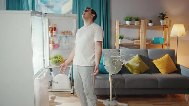 man suffering from a heat problem in the living room sticks his head in the refrigerator