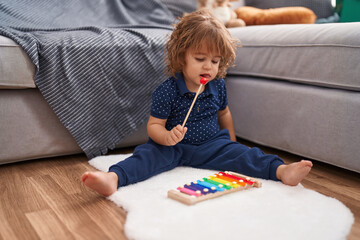 Adorable hispanic toddler playing xylophone sitting on floor at home