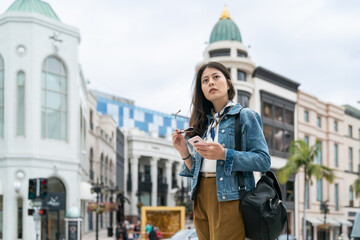 asian career woman leaving for business trip is looking around while using the mobile phone in urban area.