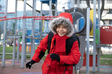 Boy in insulated jacket playing at children's playground in city. Spring is coming soon.