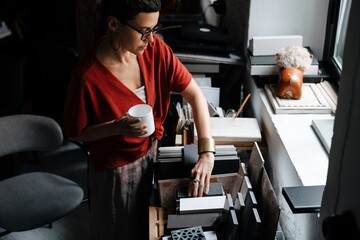 European woman drinking coffee while working with interior samples