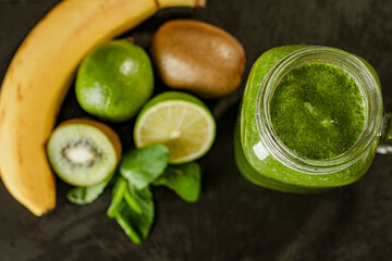 Top down view of green smoothie in glass jar and ingredients on wooden background. Selective focus 