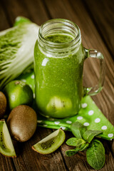 Composition of green smoothie in glass jar with straw and ingredients on wood background. Good food