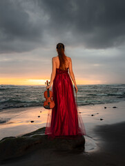 Caucasian woman with violin on the beach. Music and art concept. Slim girl wearing long red dress...