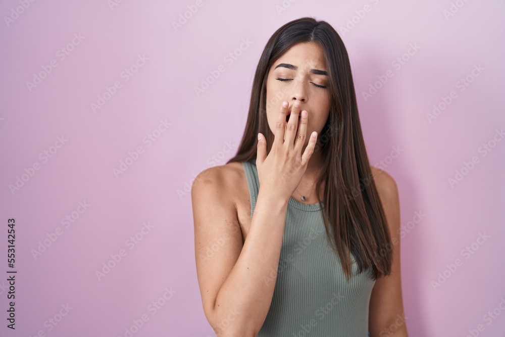 Sticker hispanic woman standing over pink background bored yawning tired covering mouth with hand. restless 