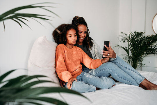Happy mother and daughter taking selfie through smart phone at home