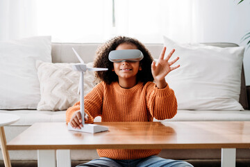 Girl wearing virtual reality simulator sitting with wind turbine model at home