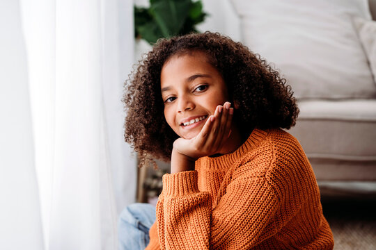 Happy Cute Girl Sitting With Hand On Chin At Home