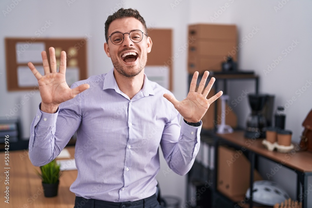 Poster Young hispanic man at the office showing and pointing up with fingers number ten while smiling confident and happy.