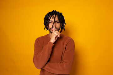 Young man with finger on lips against yellow background