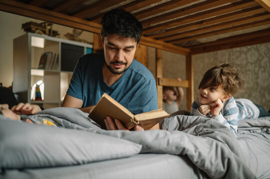 Father reads book to his sons on bed at home