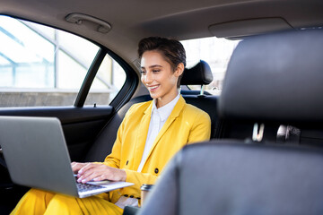 Beautiful young woman with short hair and colorful business suit remote working with laptop in a...