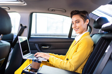 Beautiful young woman with short hair and colorful business suit remote working with laptop in a car - Corporate businesswoman on a business travel