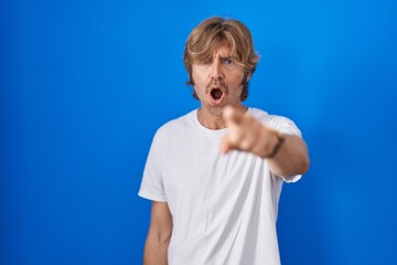 Middle age man standing over blue background pointing displeased and frustrated to the camera,...