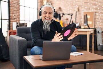 Middle age grey-haired man musician listening to music holding vinyl disc at music studio
