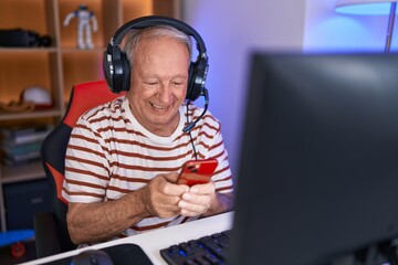 Middle age grey-haired man streamer using computer and smartphone at gaming room