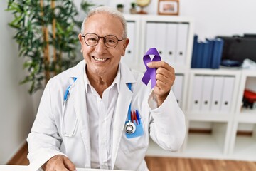 Senior doctor man holding purple ribbon awareness looking positive and happy standing and smiling...