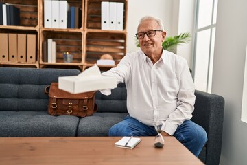 Senior man psychologist smiling confident offering napkin at psychology center