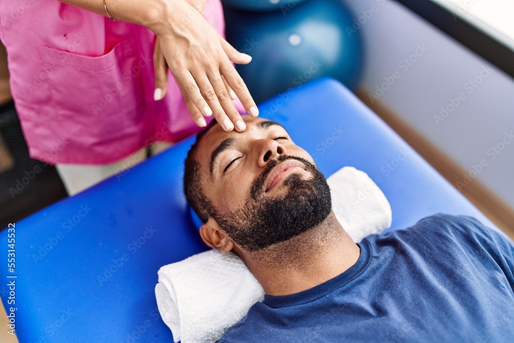 Poster man and woman wearing physiotherapist uniform having reiki session at physiotherpy clinic