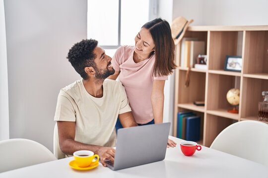 Man and woman couple sitting on table drinking coffee using laptop at home