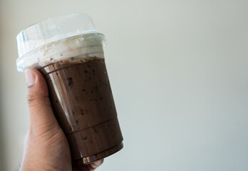 Hand hold iced mocha coffee in a take away glass with milk cream on top, cold summer drink