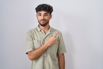 Arab man with beard standing over white background pointing with hand finger to the side showing advertisement, serious and calm face