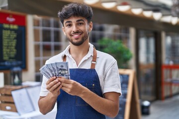 Young arab man waiter counting dollars working at restaurant
