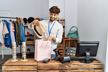 Young arab man smiling confident inserting hat on shopping bag at clothing store