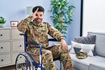 Fototapeta premium Arab man wearing camouflage army uniform sitting on wheelchair doing ok gesture with hand smiling, eye looking through fingers with happy face.