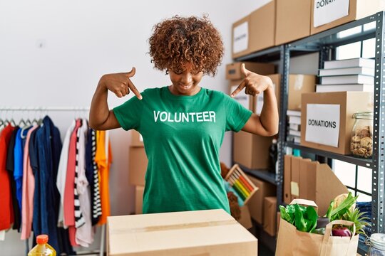 Young african american woman pointing with fingers to volunteer uniform at charity center