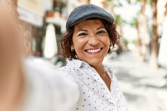 Middle age latin woman smiling happy making selfie by the camera at the city.