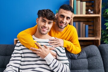 Two man couple hugging each other sitting on sofa at home