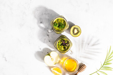 Green detox drink in other glass jars with ingredients and shadows on a white background, top view.