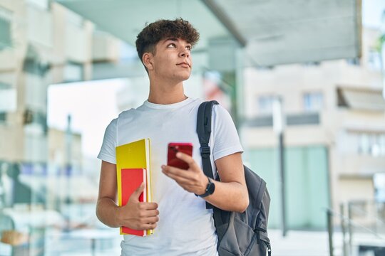 Young Hispanic Teenager Student Using Smartphone Holding Books At University