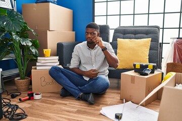 African american man sitting on the floor at new home mouth and lips shut as zip with fingers. secret and silent, taboo talking