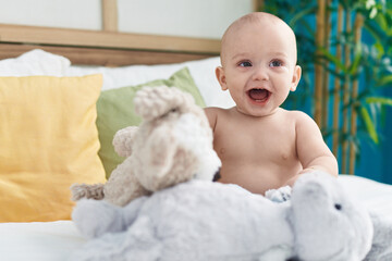 Adorable caucasian baby sitting on bed with dolls smiling at bedroom