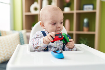 Adorable caucasian baby palying with cars toy sitting on highchair at home