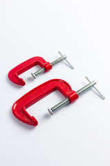 Two red metal clamps of different sizes on a white background. Tools for repair work and DIY projects. Construction, craft, work with wood products.